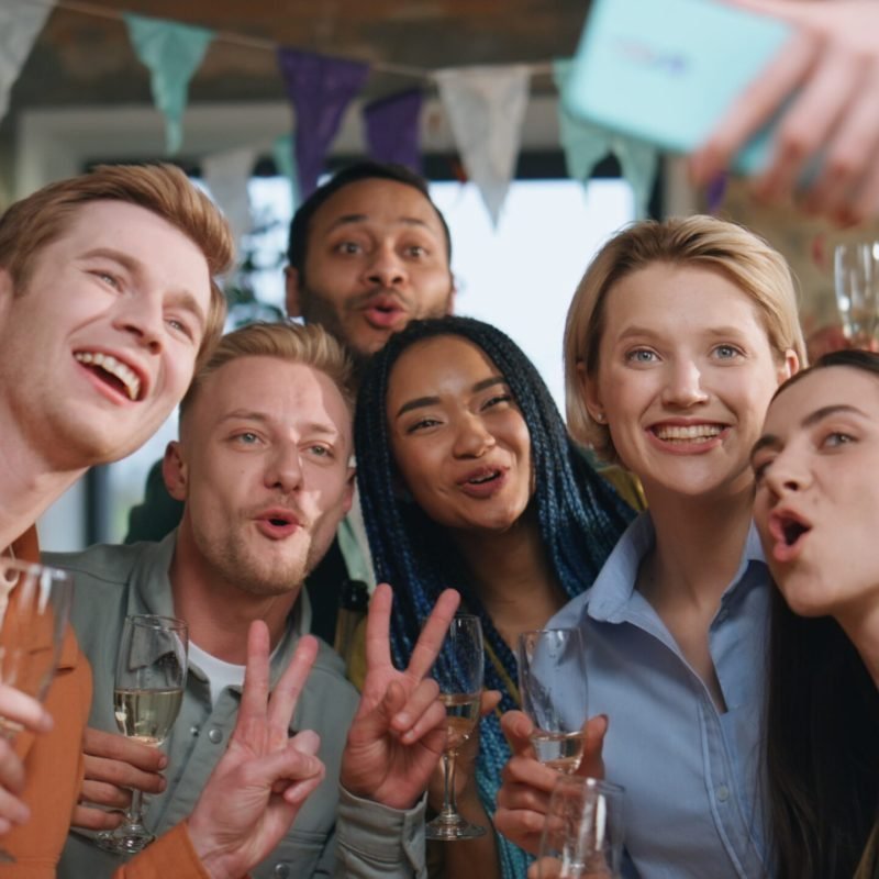 Team making selfie party for company anniversary close up. Friends laughing Team making selfie at party for company anniversary close up. Cheerful friends looking on smartphone photo laughing together. Happy colleagues holding wine glasses celebrating business success indoors
